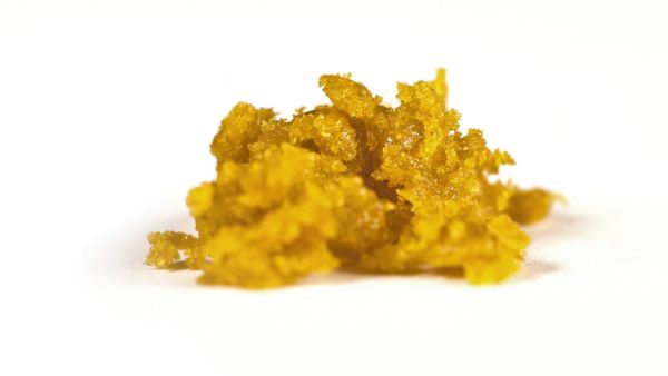 A close-up of a small pile of yellow, crumbly concentrate on a white background.